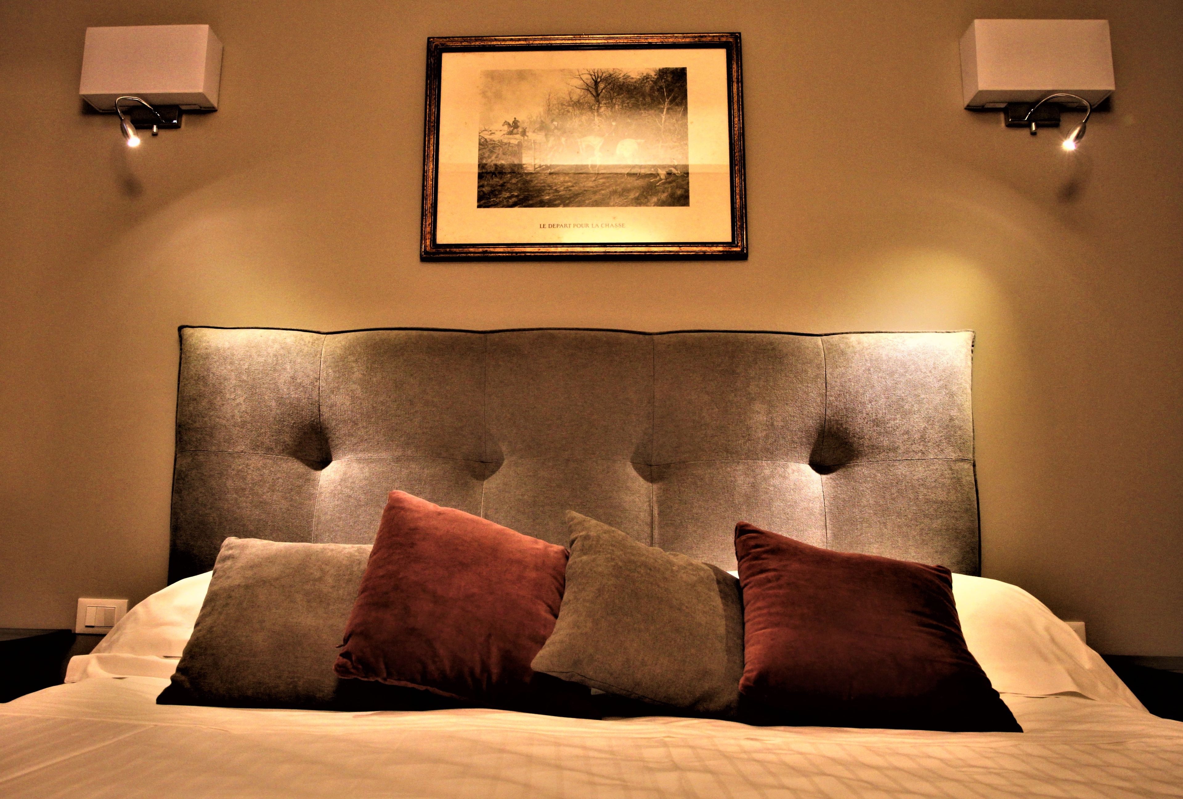 A bedroom with a tufted headboard, a framed picture on the wall, and two wall-mounted lamps.