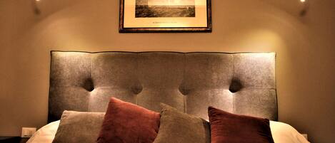 A bedroom with a tufted headboard, a framed picture on the wall, and two wall-mounted lamps.