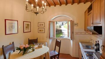 Un comedor con una mesa dispuesta para dos, una araña y un ventanal con una puerta abierta hacia el exterior.