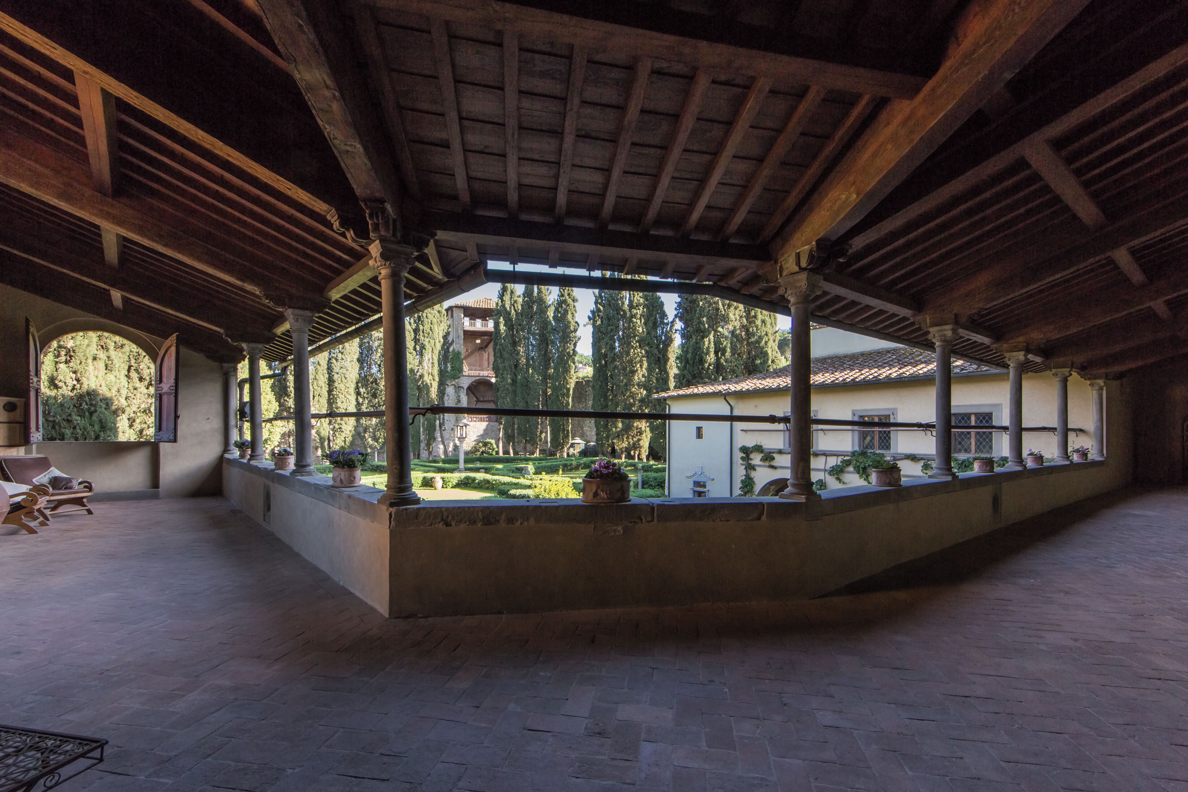 Un patio abierto con techo de madera, columnas y plantas en macetas.