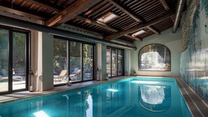 Una piscina interior con paredes de vidrio transparente, vigas de madera y ventanas amplias.