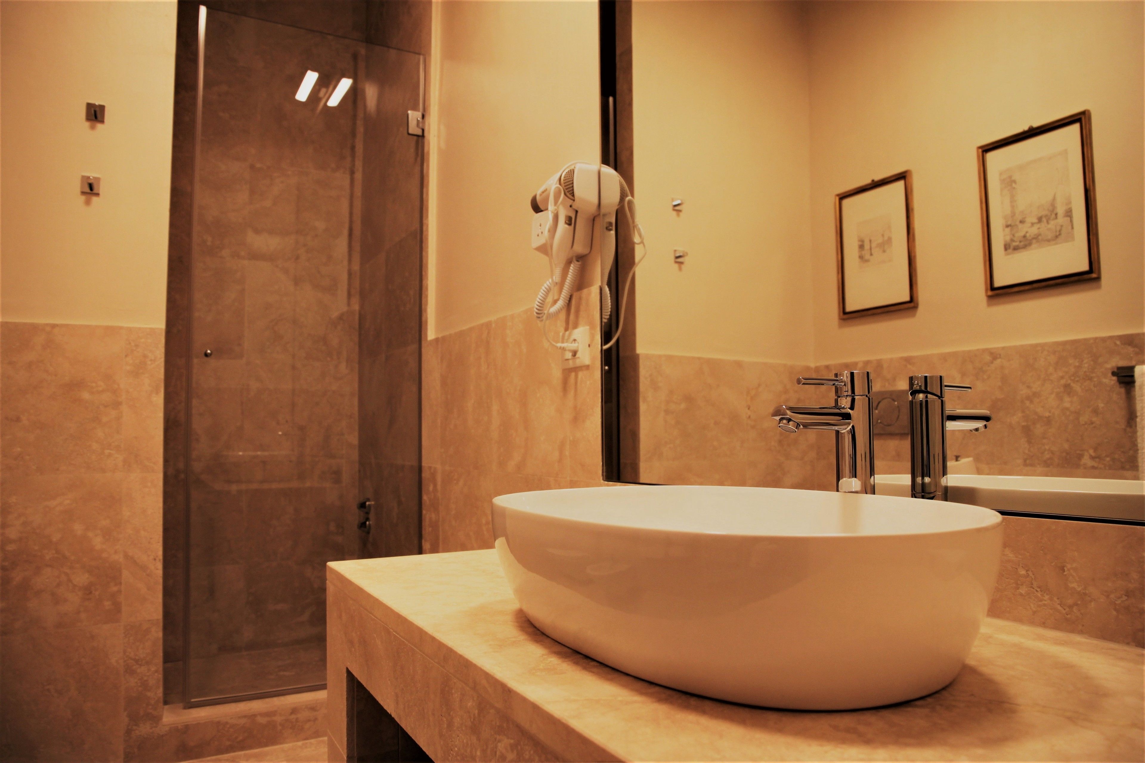 A modern bathroom with a large oval sink, a glass shower enclosure, and framed artwork on the wall.