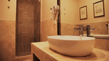 A modern bathroom with a large oval sink, a glass shower enclosure, and framed artwork on the wall.
