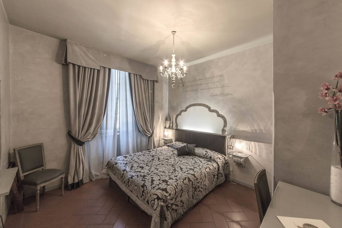 A bedroom with a large bed, a chandelier, a desk, and a chair.