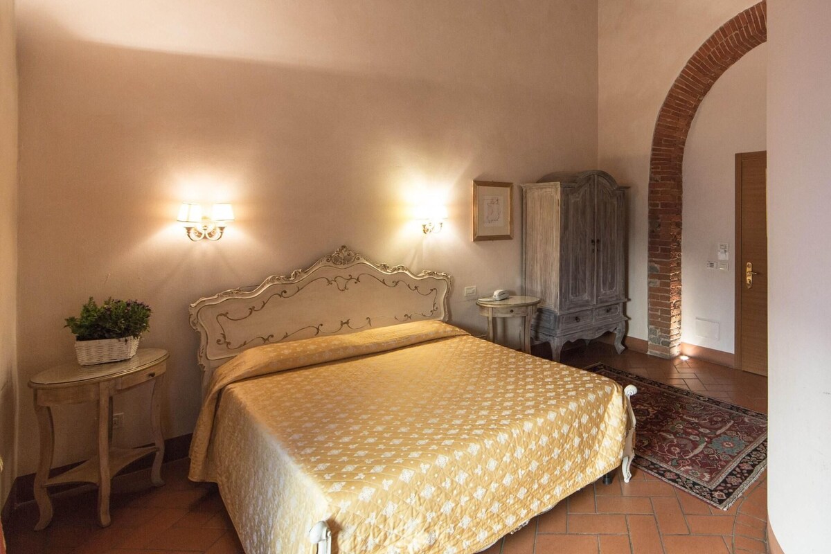 Un dormitorio con cama, mesitas de noche, lámpara, armario y un arco de ladrillo.