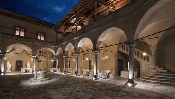 Un patio interior con suelo de piedra, columnas en arco y mesas dispuestas para comer.