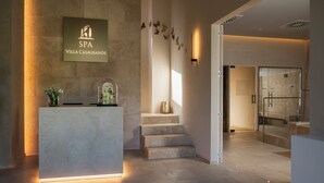Una recepción moderna con mostrador de piedra, un cartel que indica SPA VILLA CASAGRANDE y una escalera que conduce a una puerta de cristal.