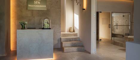 A modern reception area with a stone counter, a sign for SPA VILLA CASAGRANDE, and a staircase leading to a glass door.
