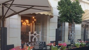 An outdoor seating area with tables and chairs, a large umbrella, and a potted plant. - Hotel Castillo (Palma del Rio)