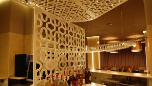 A bar area with a decorative white partition, a variety of liquor bottles, and a modern chandelier. - Hotel Castillo (Palma del Rio)