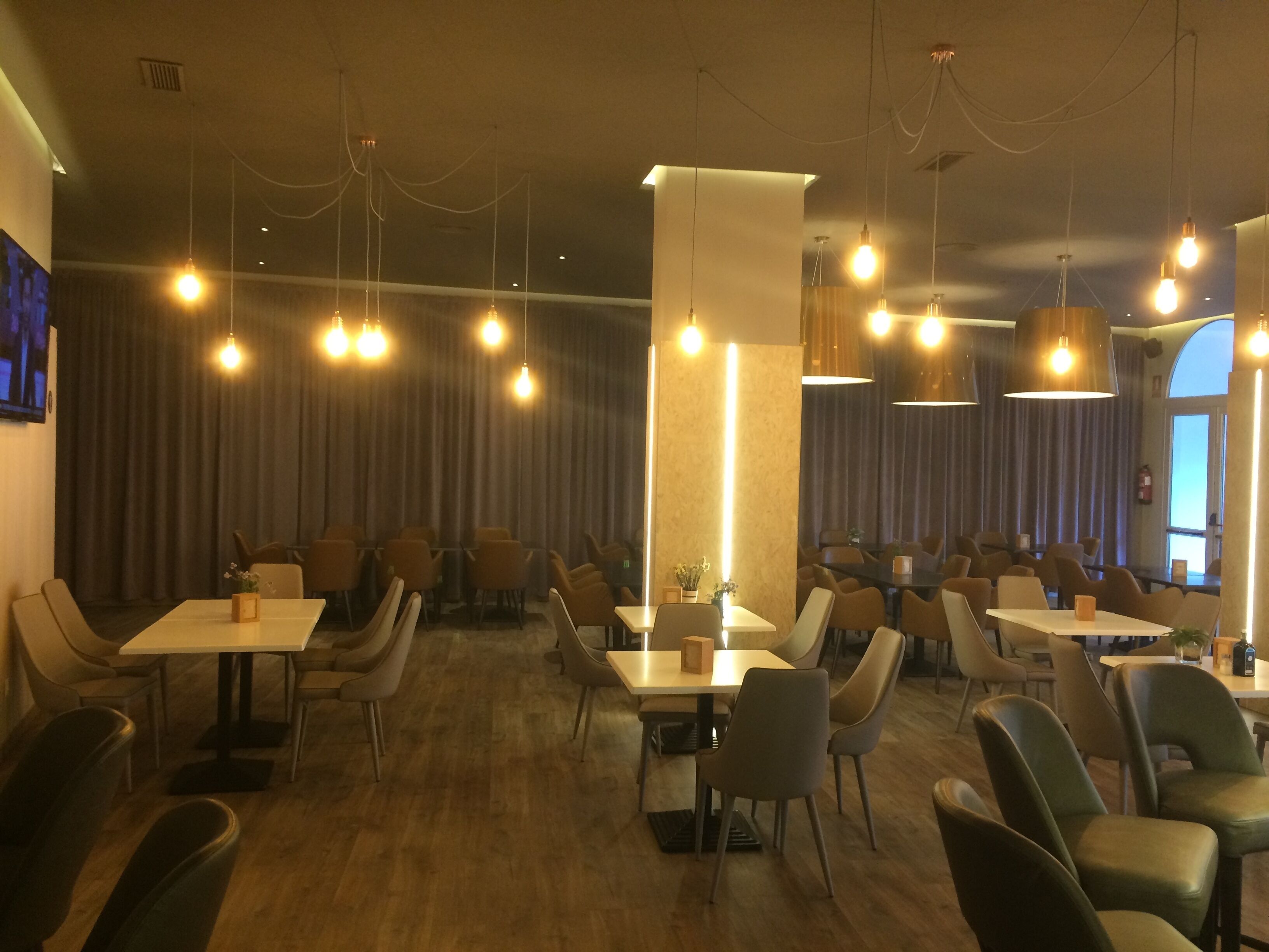 A restaurant with multiple tables and chairs, pendant lighting, and a modern interior design.