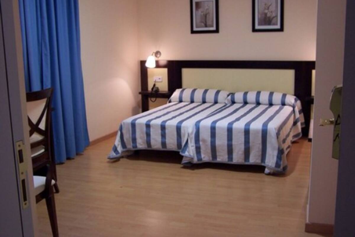 A hotel room with a double bed, a nightstand with a lamp, and two framed pictures on the wall.