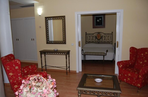 A room with a bed, two armchairs, a small table, a mirror, and a door leading to another room.