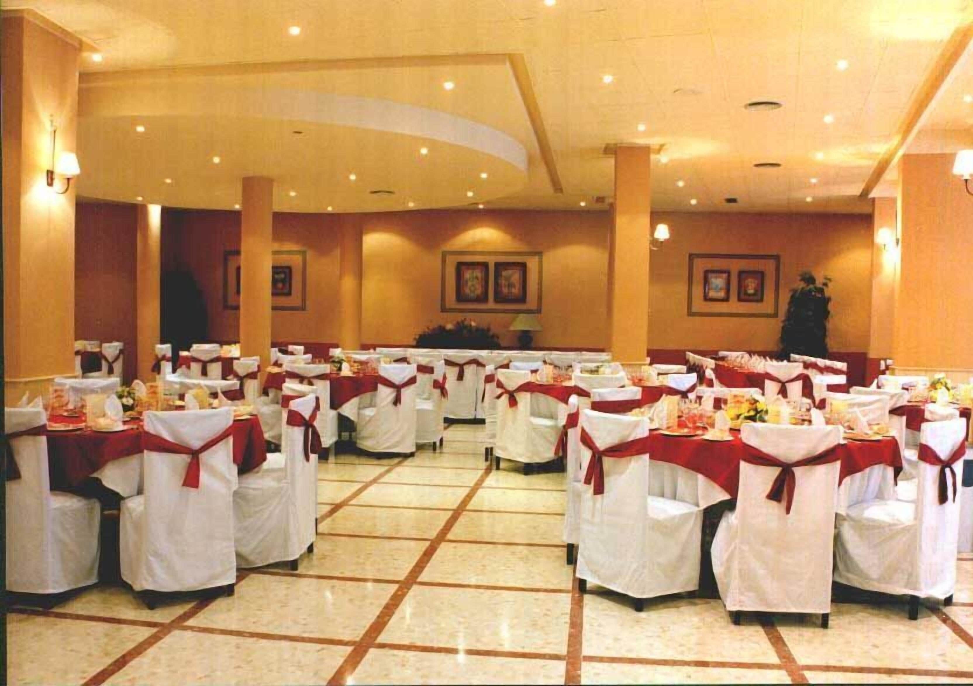 Un saló de banquetes amb taules rodones, cadires blanques i cintes vermelles.