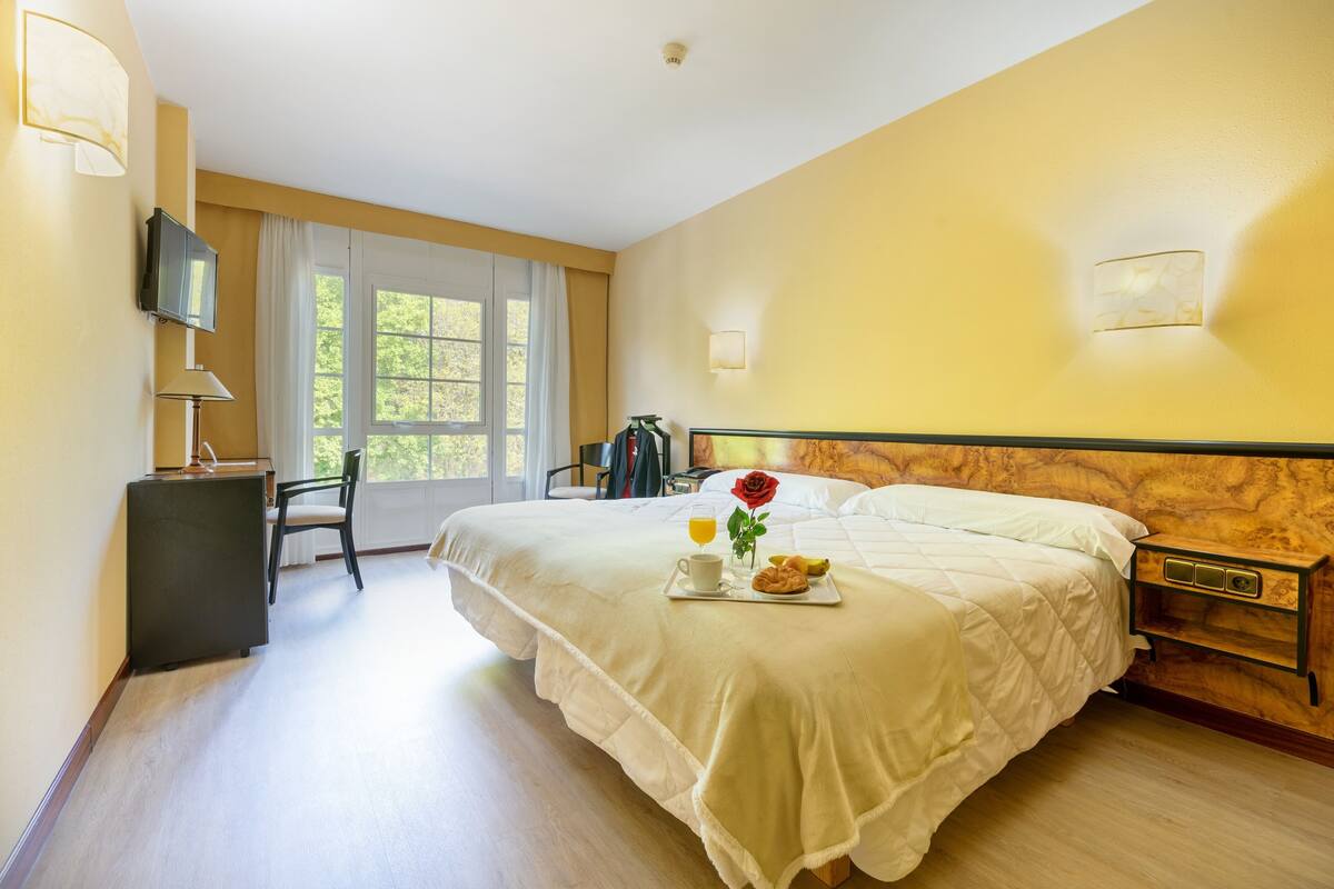 Ein Hotelzimmer mit einem großen Bett, einem Schreibtisch mit Stuhl, einem Fernseher und einem Fenster mit Vorhängen.