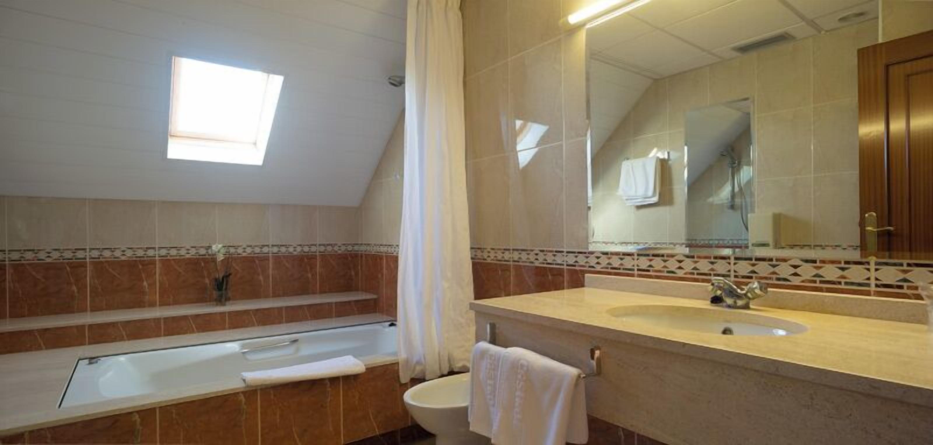 Une salle de bain avec une baignoire, un lavabo et des toilettes. Il y a une fenêtre qui laisse entrer la lumière naturelle et un miroir au-dessus du lavabo.