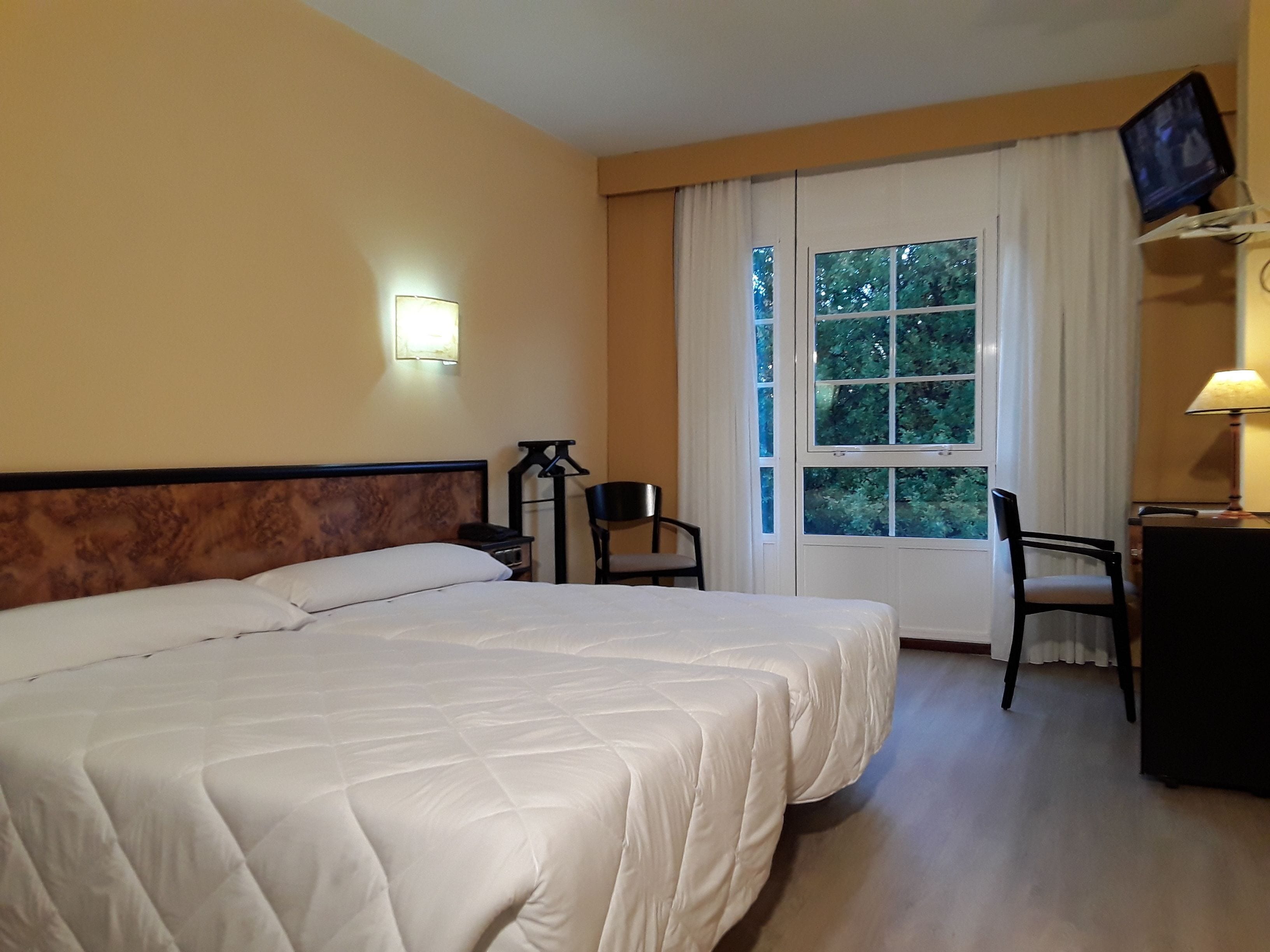 A hotel room with a large bed, a desk with a chair, a television mounted on the wall, and a window with curtains.