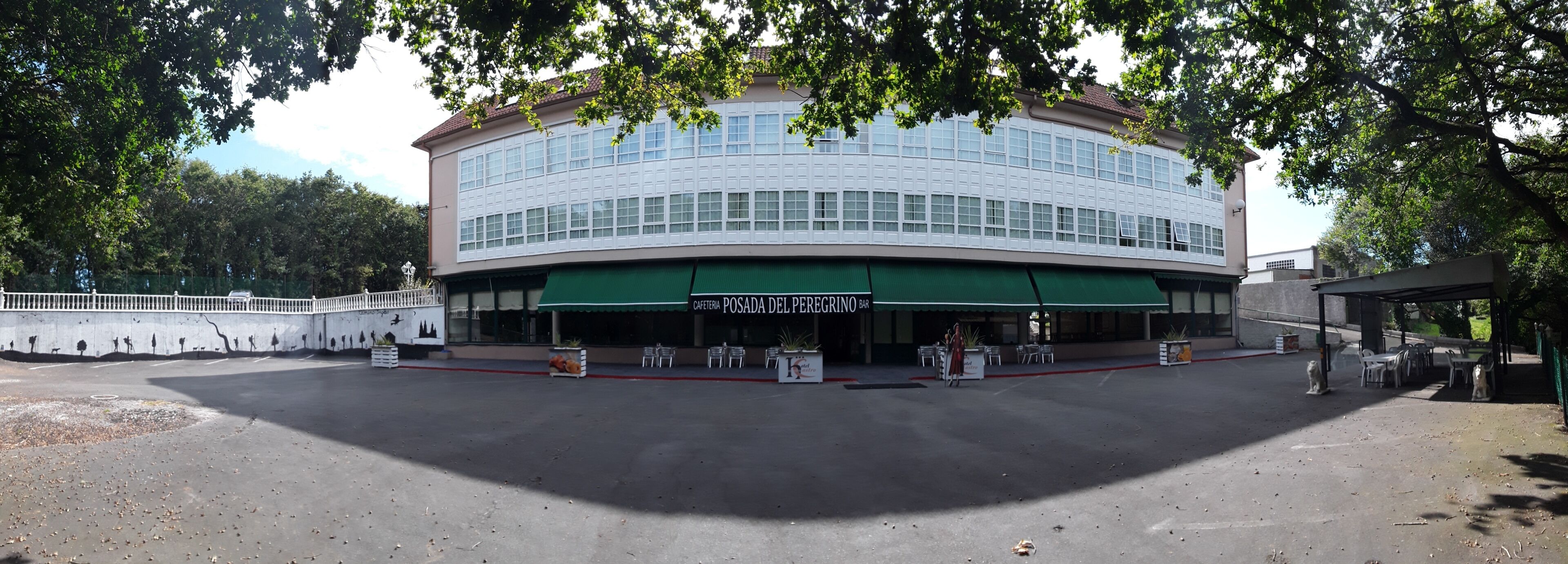 Un edificio con toldo verde, un letrero que dice "CAFETERIA POSADA DEL PEREGRINO BAR" y mesas al aire libre.