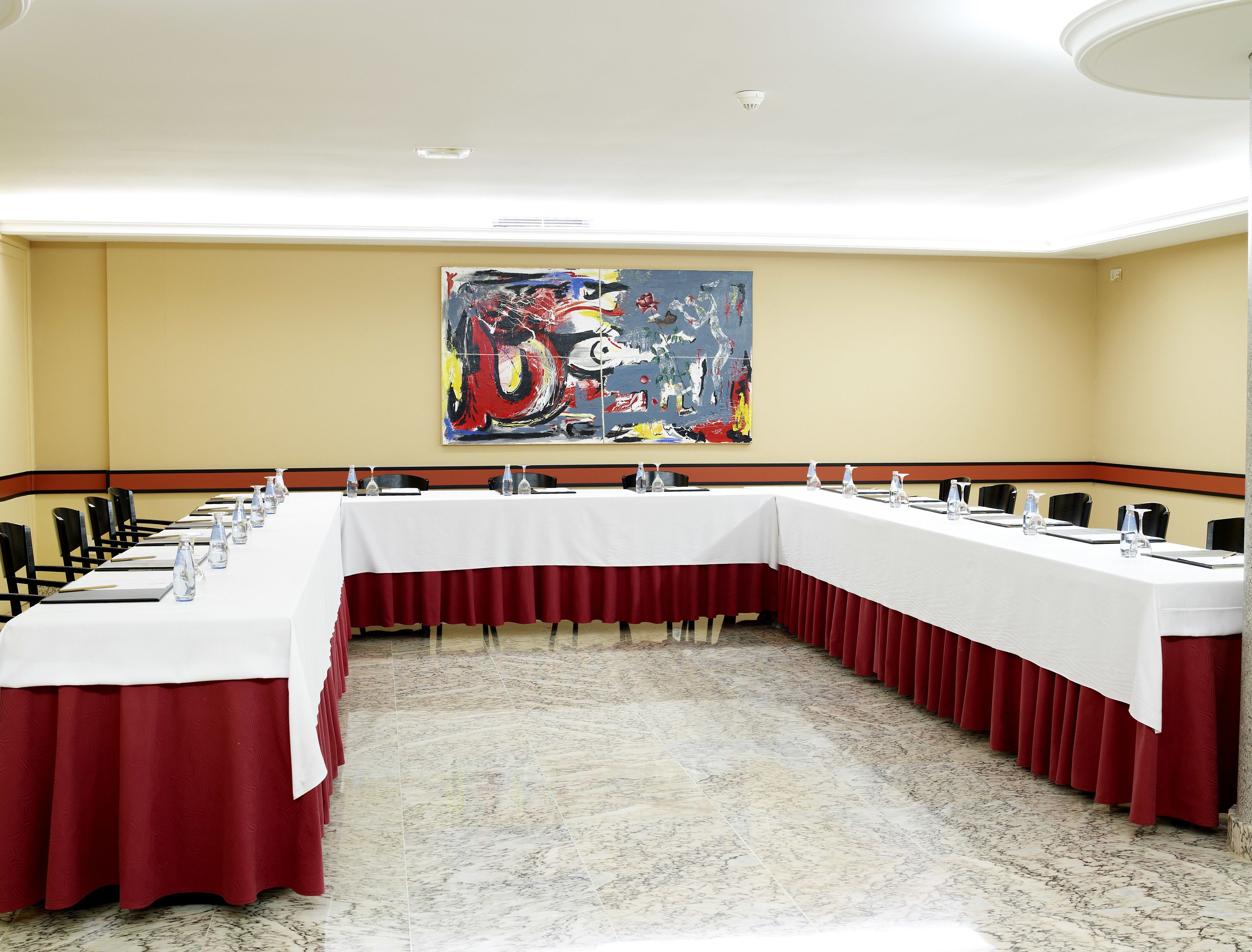 Un salón de conferencias con una larga mesa, sillas y un cuadro abstracto de grandes dimensiones en la pared.