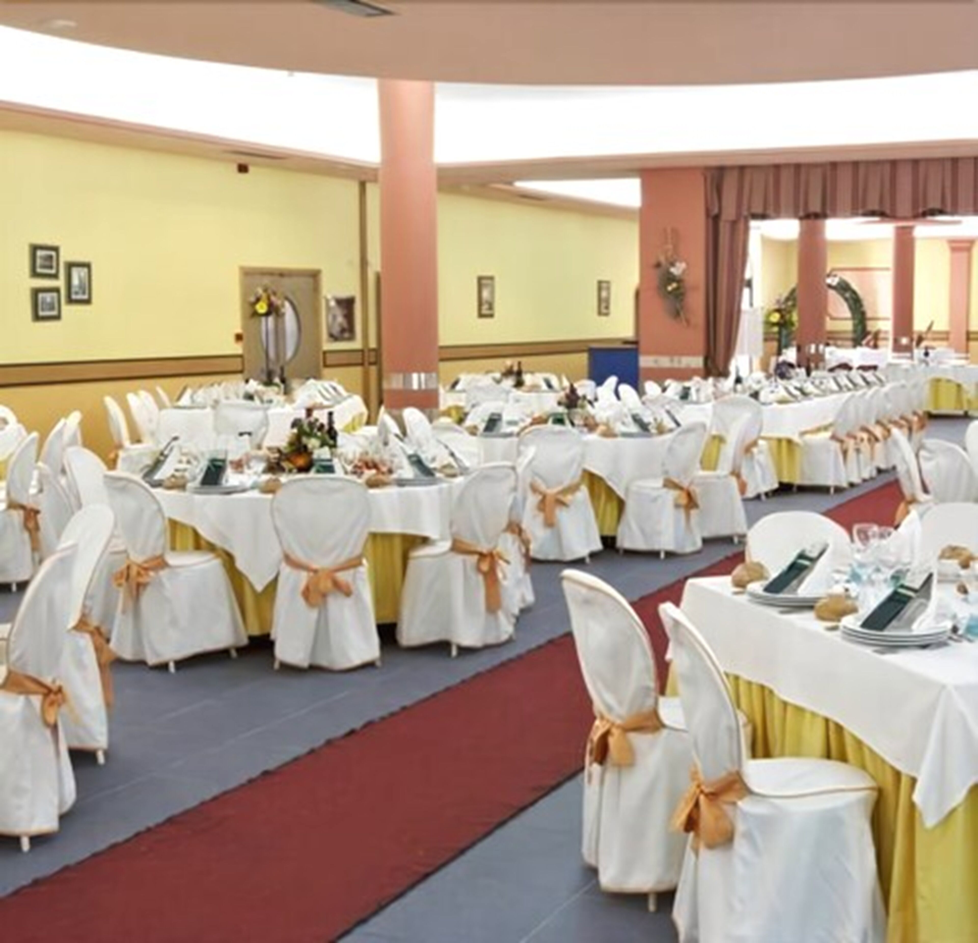 A banquet hall with round tables covered in white tablecloths and gold sashes, arranged in rows.