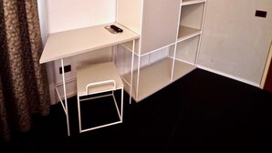 A compact room with a white desk, a mounted TV, and a wardrobe with multiple shelves. - Hotel Centrale (Mestre)