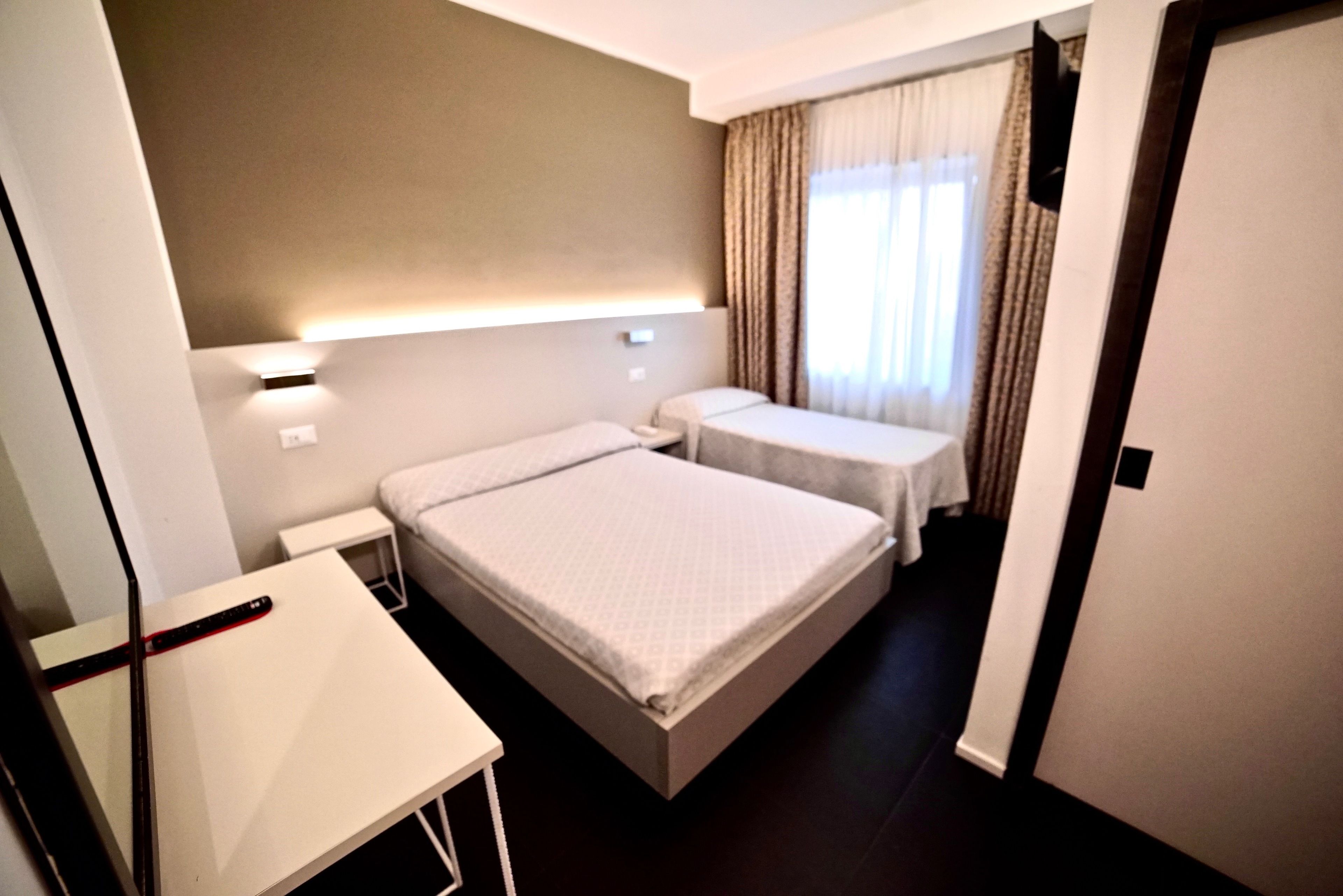 A hotel room with a single bed, a small table, and a desk with a computer.