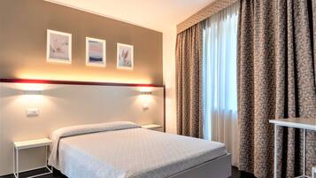 A hotel room with a bed, bedside tables, wall-mounted lights, and curtains.
