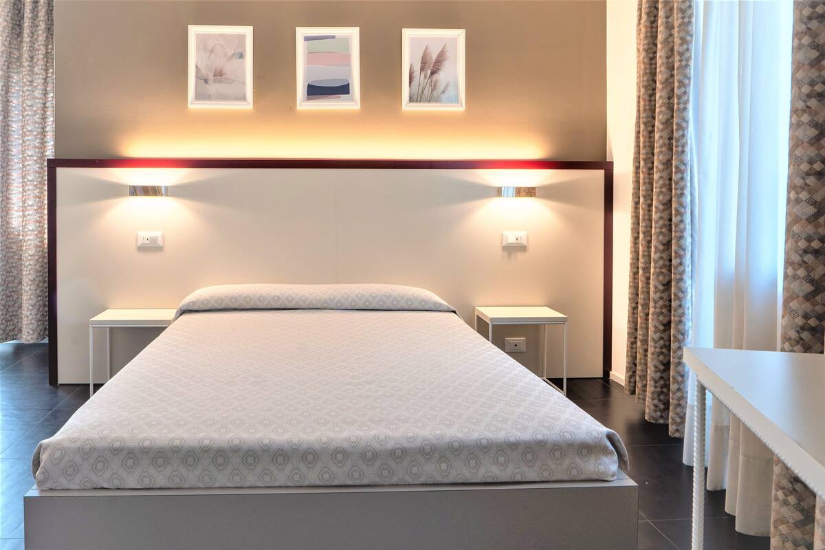 A neatly made bed with a patterned bedspread, two bedside tables with lamps, and three framed pictures on the wall above the bed.