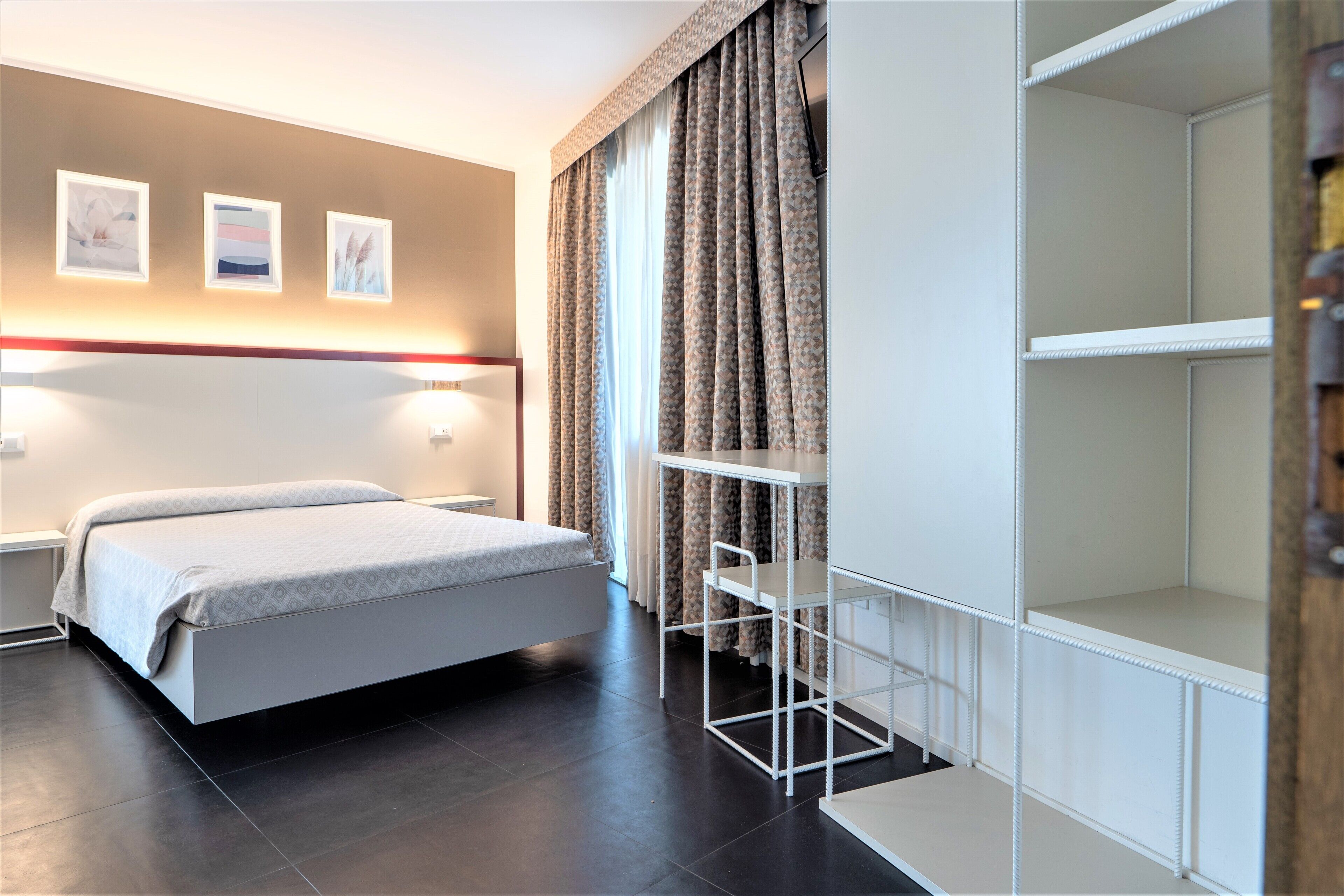 A modern hotel room with a bed, a desk, and a wardrobe.