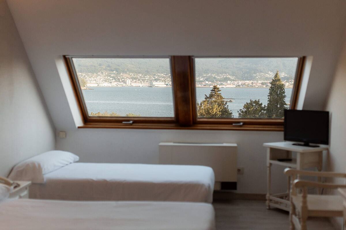 A bedroom with two beds, a TV, and a view of a body of water and cityscape.