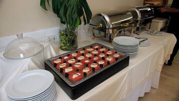 Una mesa de buffet con una variedad de platos, incluyendo una bandeja de ensalada de tomate y mozzarella, y una máquina de café.