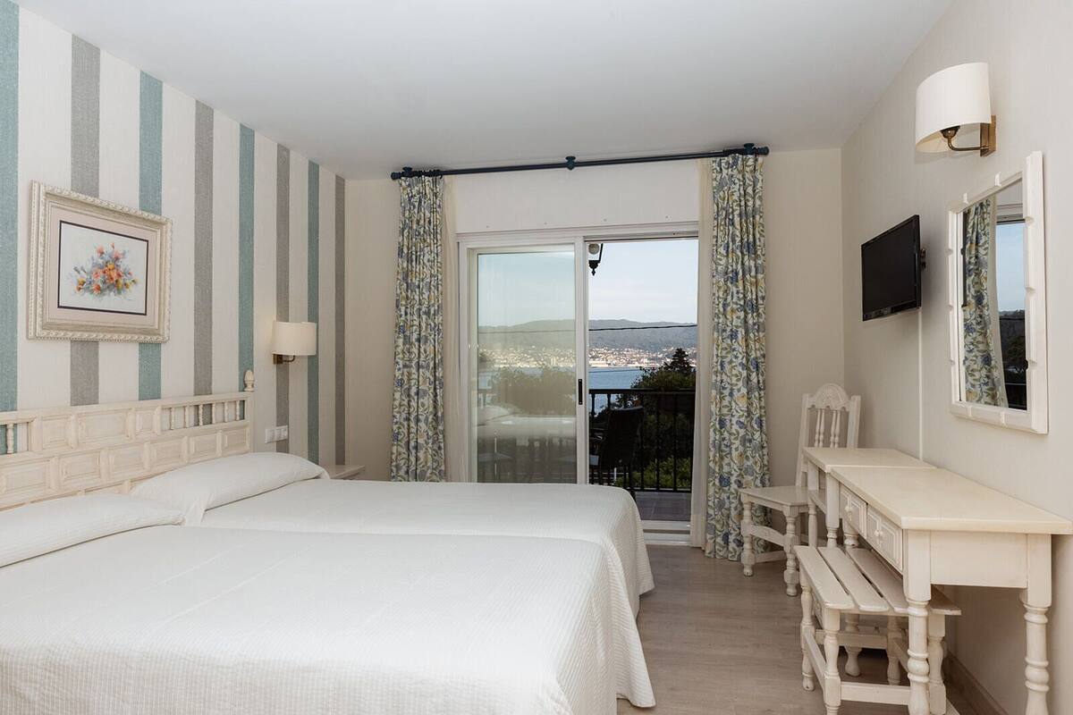 A hotel room with a large bed, a desk, and a balcony with curtains.