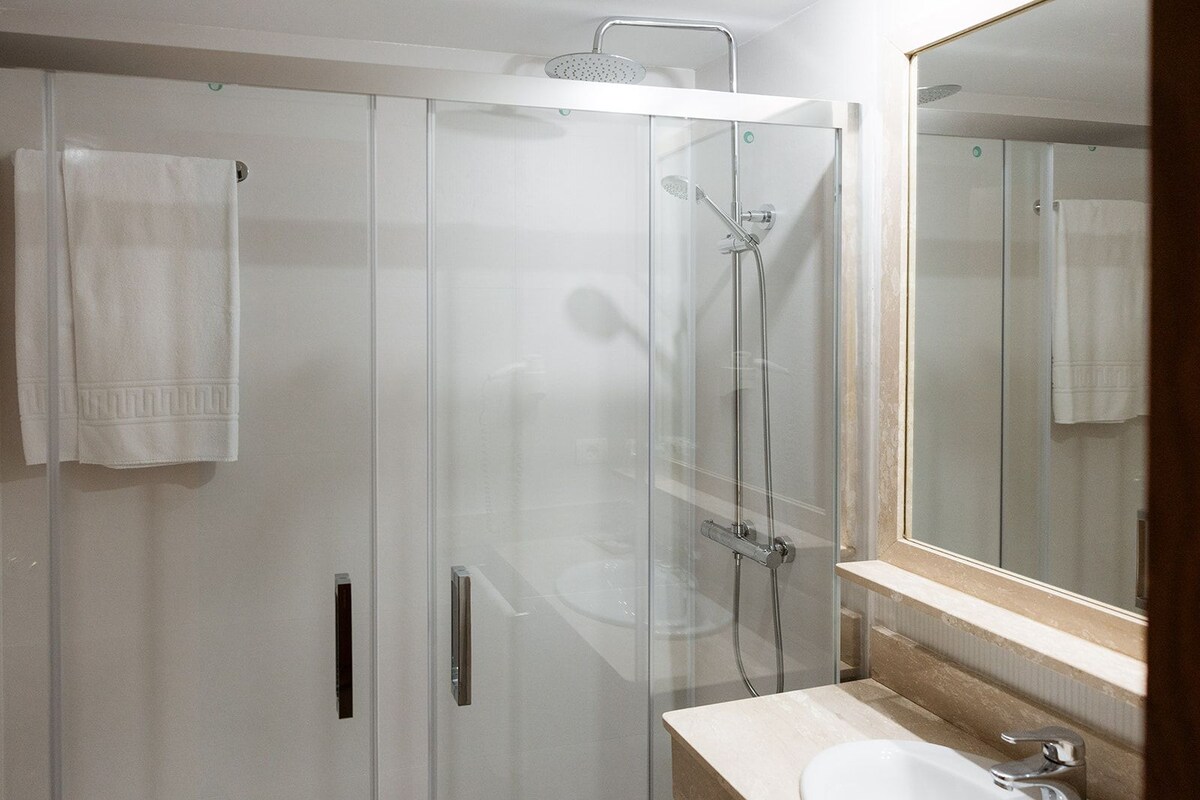 Un baño moderno con ducha de vidrio, lavabo blanco y un espejo grande.
