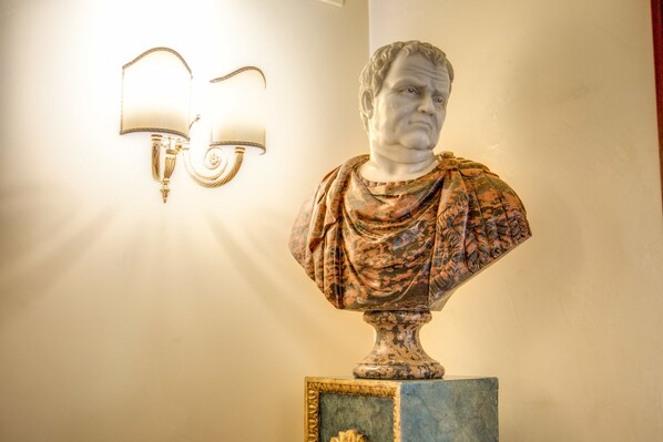 A bust sculpture on a pedestal with a marble base, positioned against a wall with two wall-mounted lamps. - Aurelius Art Gallery Hotel (Rome)