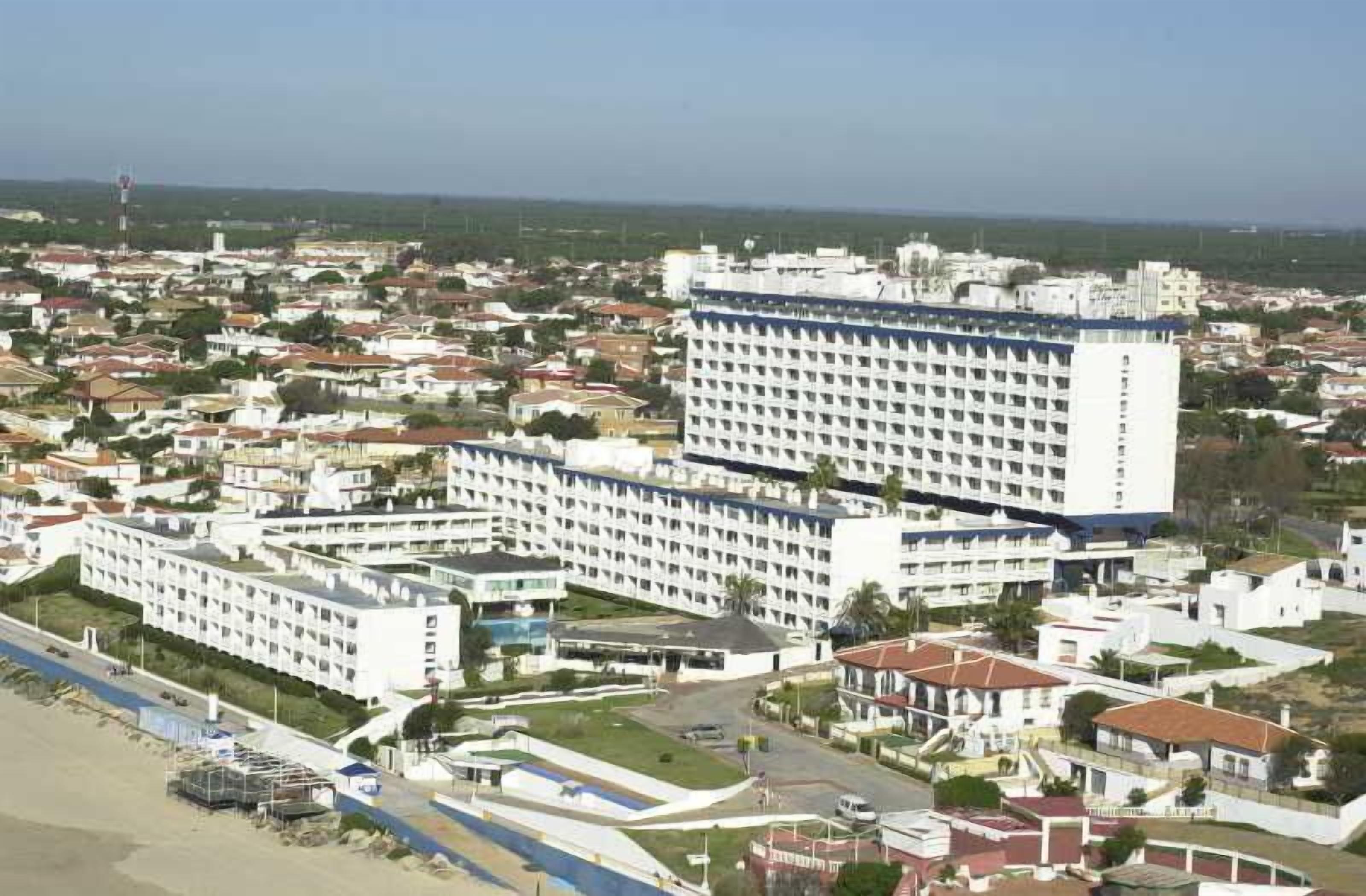 A large hotel complex with multiple buildings, a beach area, and a clear view of the surrounding cityscape.