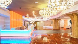 A hotel lobby with a reception desk, seating area, and a chandelier. - Flamero (Almonte)