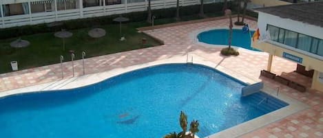 Una piscina con solárium empedrado, rodeada por un edificio con varios balcones.