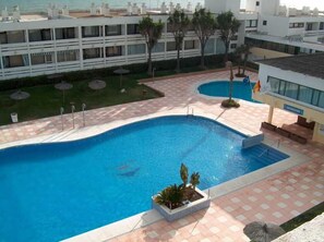 A swimming pool with a tiled deck, surrounded by a building with multiple balconies. - Flamero (Almonte)