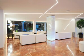 A modern lobby with a marble floor, white sofas, and a large potted plant. - Flamero (Almonte)