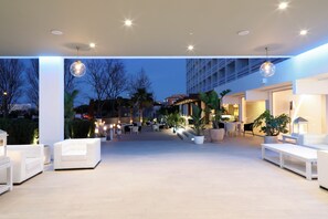 An outdoor lounge area with seating and tables, surrounded by potted plants and trees.