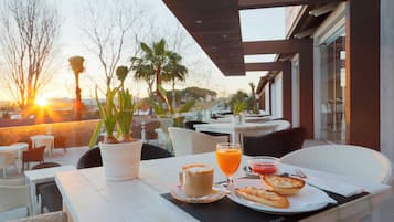 An outdoor dining area with a table set for two, featuring a beverage, a pastry, and a plant.