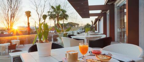Un área de comedor al aire libre con una mesa dispuesta para dos personas, que incluye una bebida, un pastel y una planta.