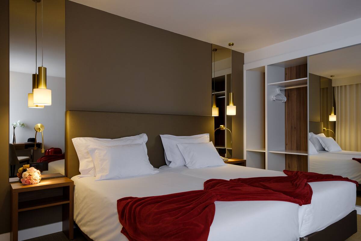 A modern hotel room with a large bed, bedside tables, a mirror, and a wardrobe.