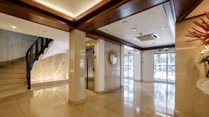 A modern hotel lobby with a marble floor, a staircase, an elevator, and a reception desk. - Hotel Regina (Ourem)
