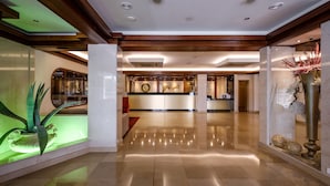 A spacious lobby with a polished floor, a reception desk, and a decorative plant display. - Hotel Regina (Ourem)
