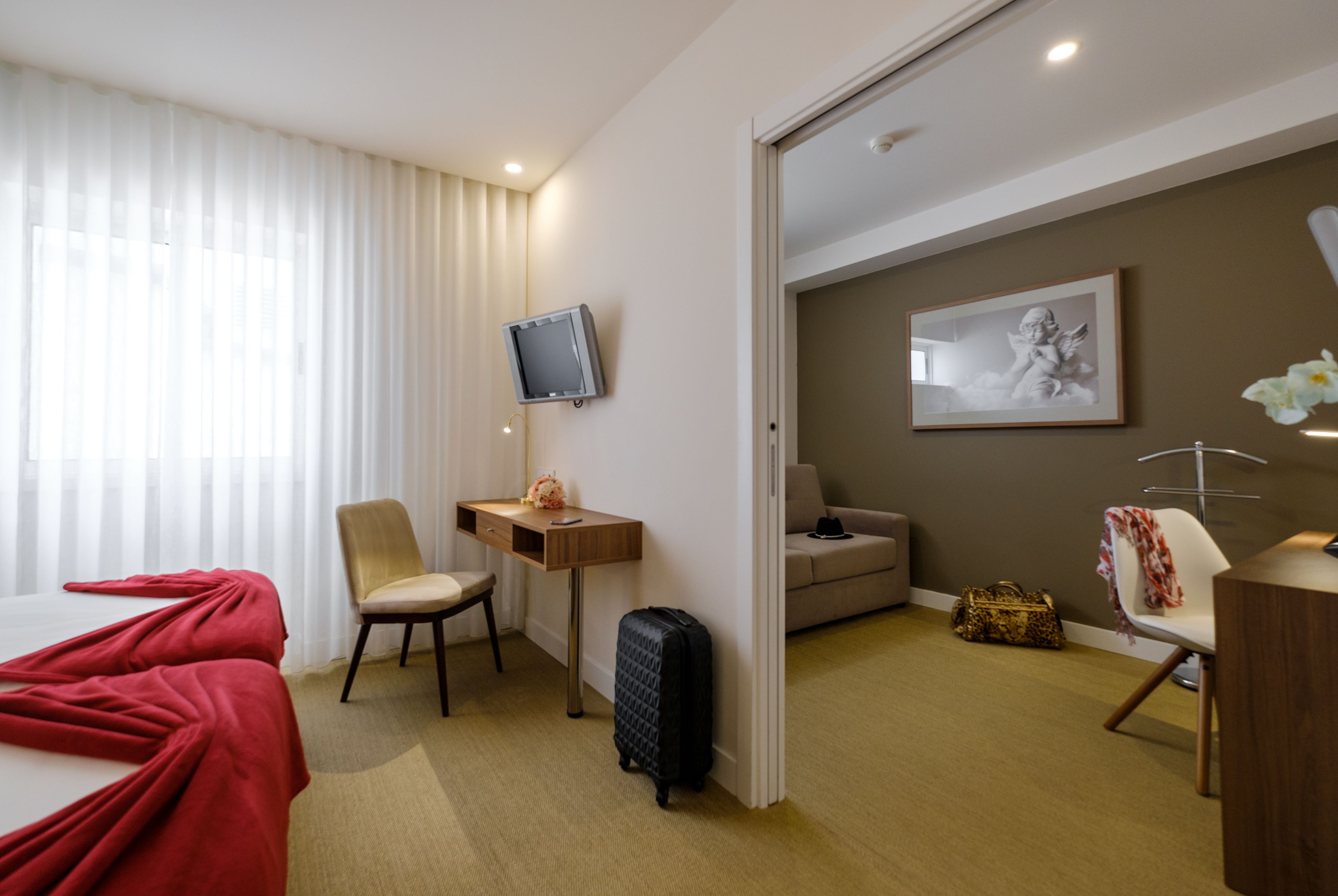 Ett hotellrum med en säng, ett skrivbord, en stol, en tv, en soffa och en resväska.