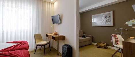 Ett hotellrum med en säng, ett skrivbord, en stol, en tv, en soffa och en resväska.