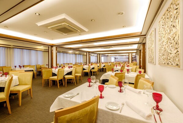A spacious dining area with multiple tables set for dining, featuring white tablecloths and red wine glasses.