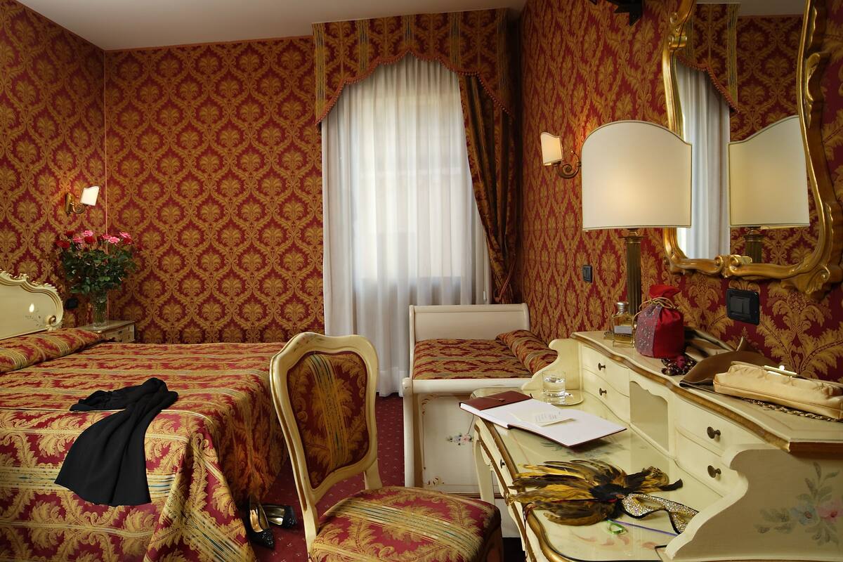Een hotelkamer met twee bedden, een bureau, een stoel, een kaptafel met spiegel en een raam met gordijnen.