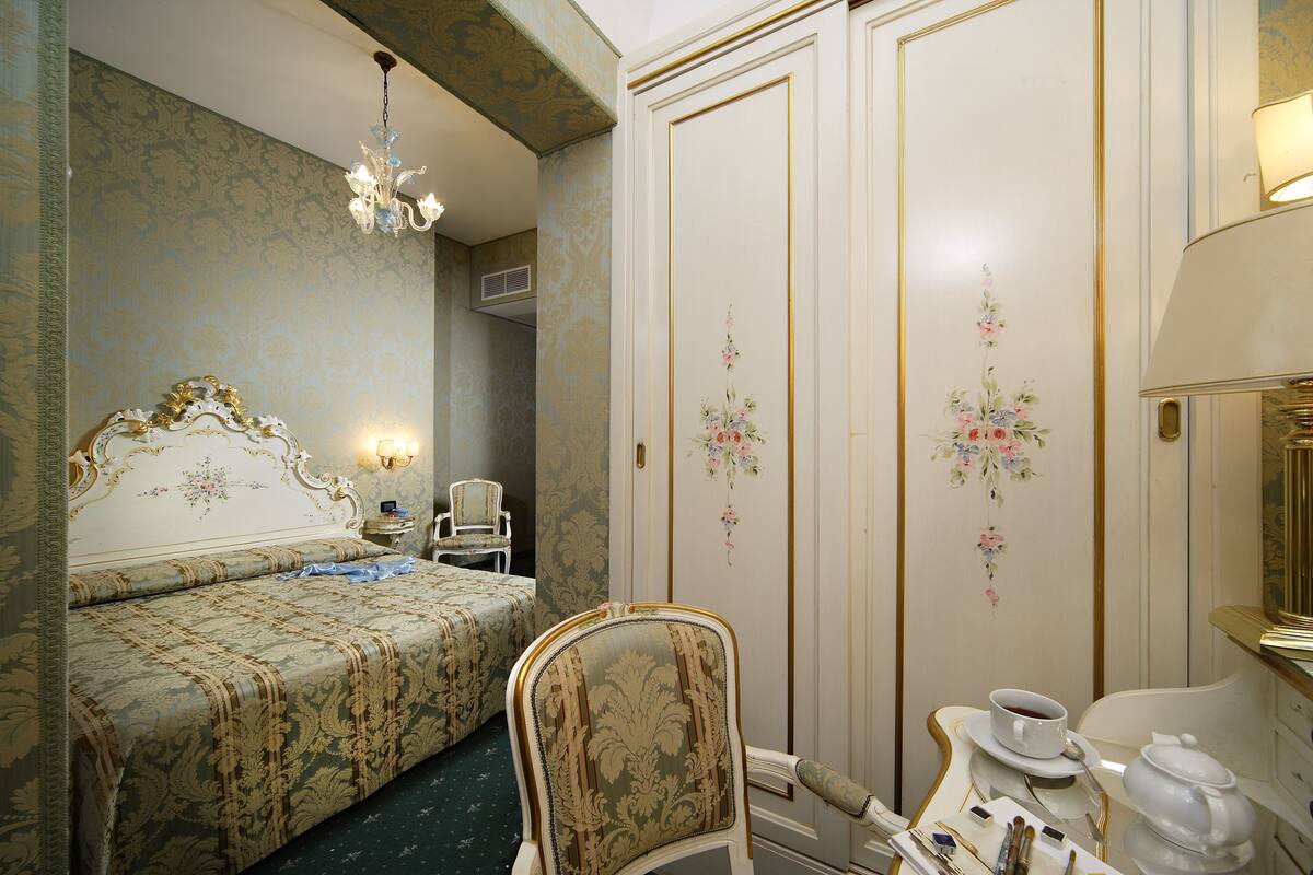 Een kamer met een bed, een stoel, een tafel met theepot en kopjes, en een wand met bloemdecoraties.